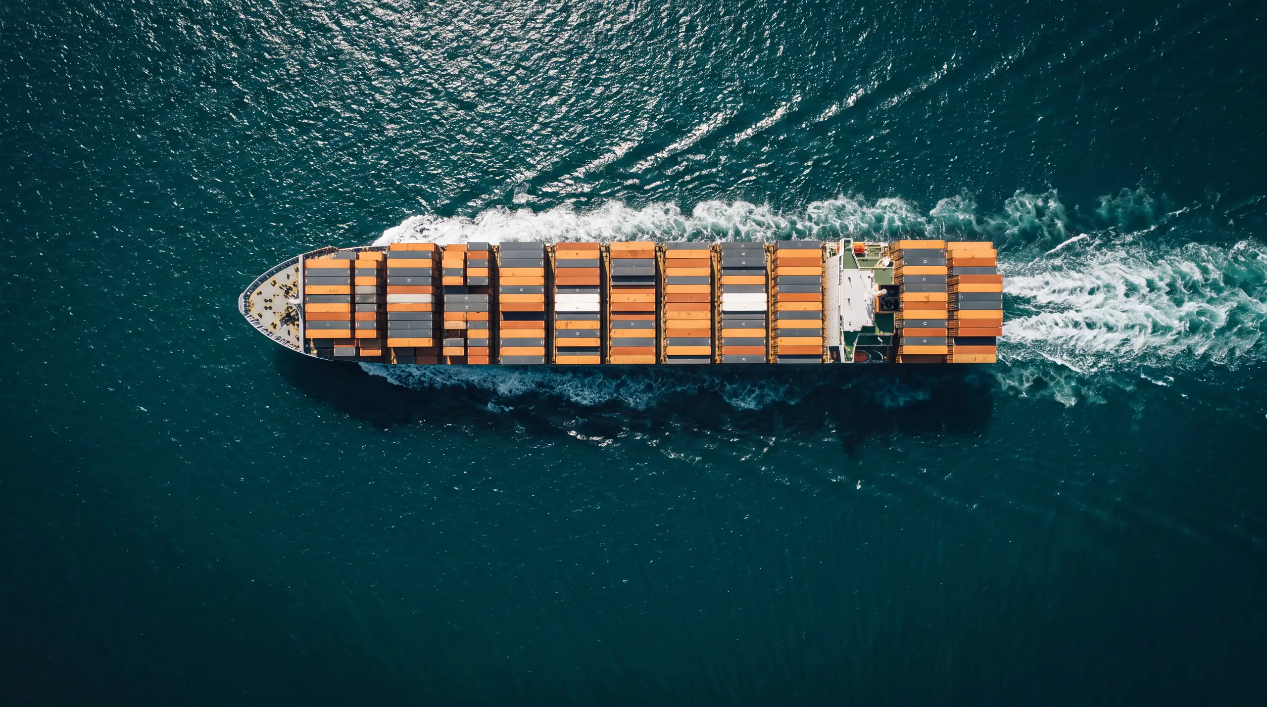 Container ship seen from above, crossing open teal water