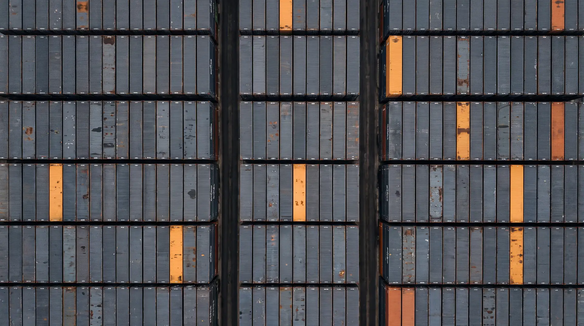 Container yard seen from directly above, a grid of charcoal roofs with a few amber ones